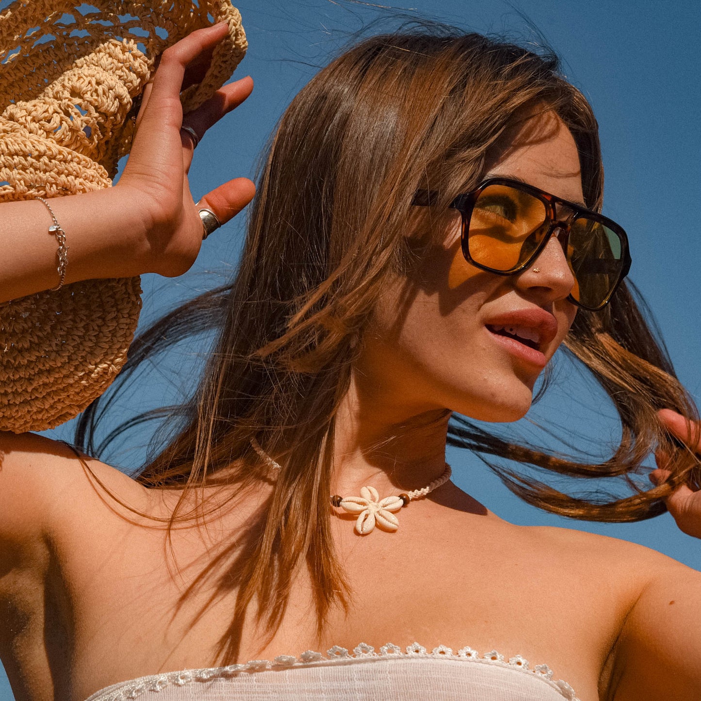 Woman with sunglasses and a straw hat against a clear blue sky wearing the natural blues necklace