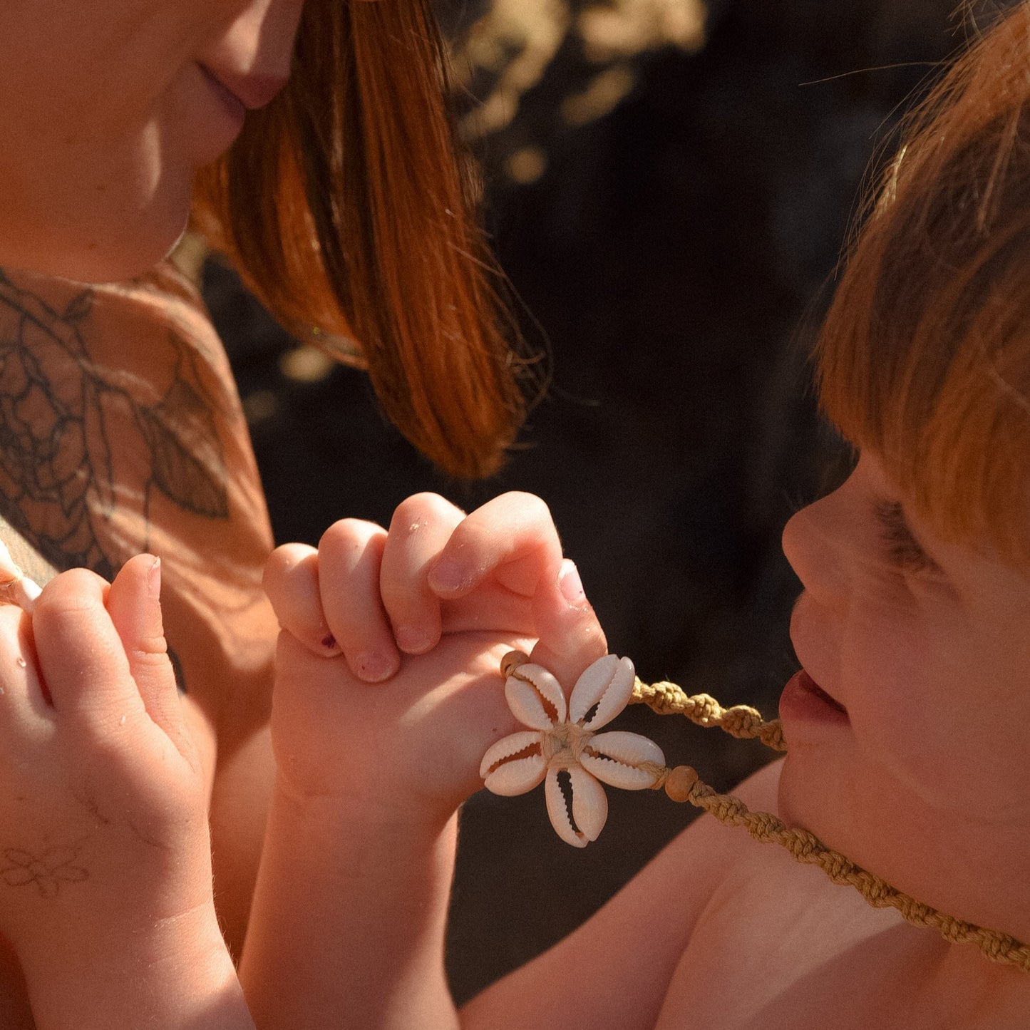 Woman and child holding hands with a necklace featuring a flower pendant.
