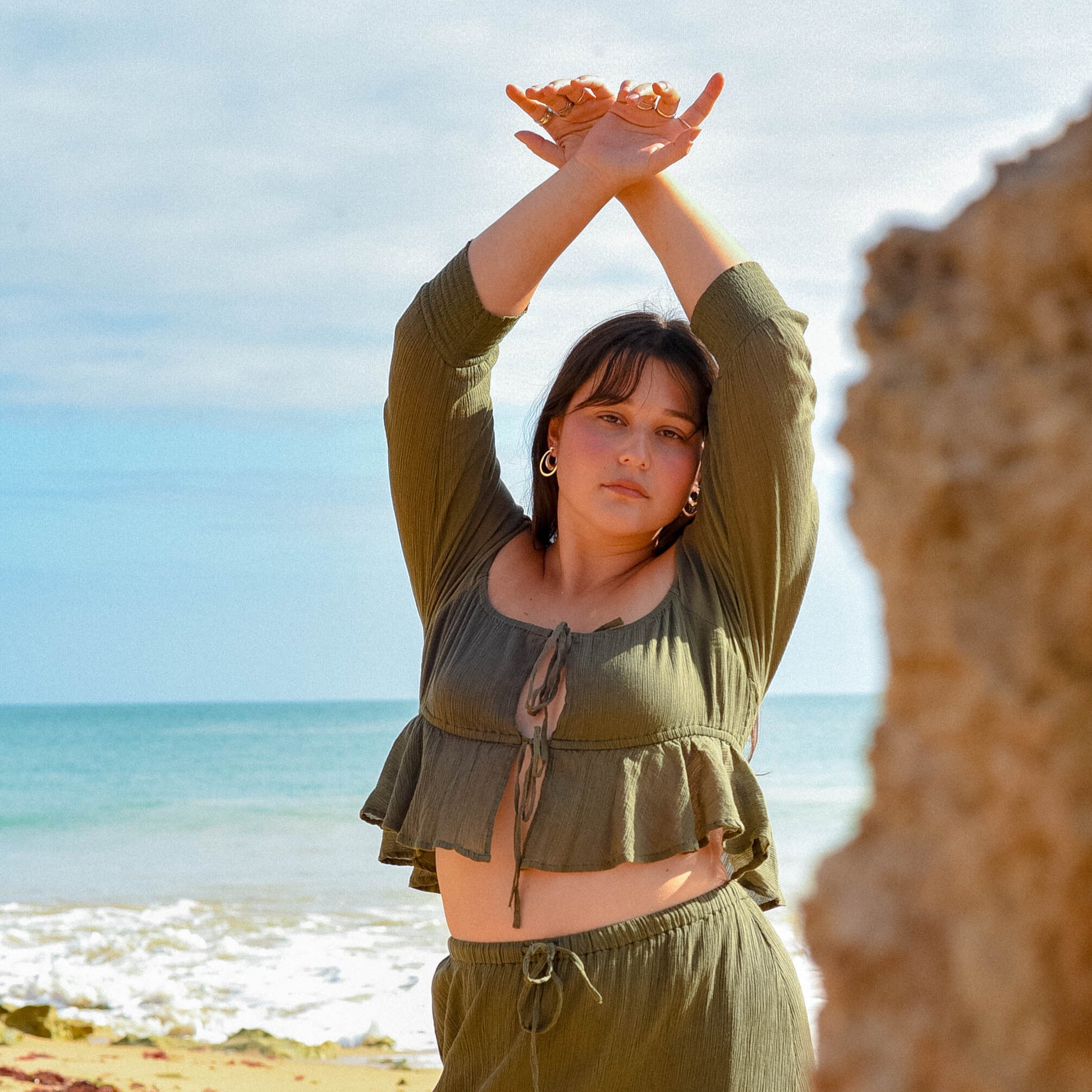 Woman in green outfit standing on a beach with ocean view