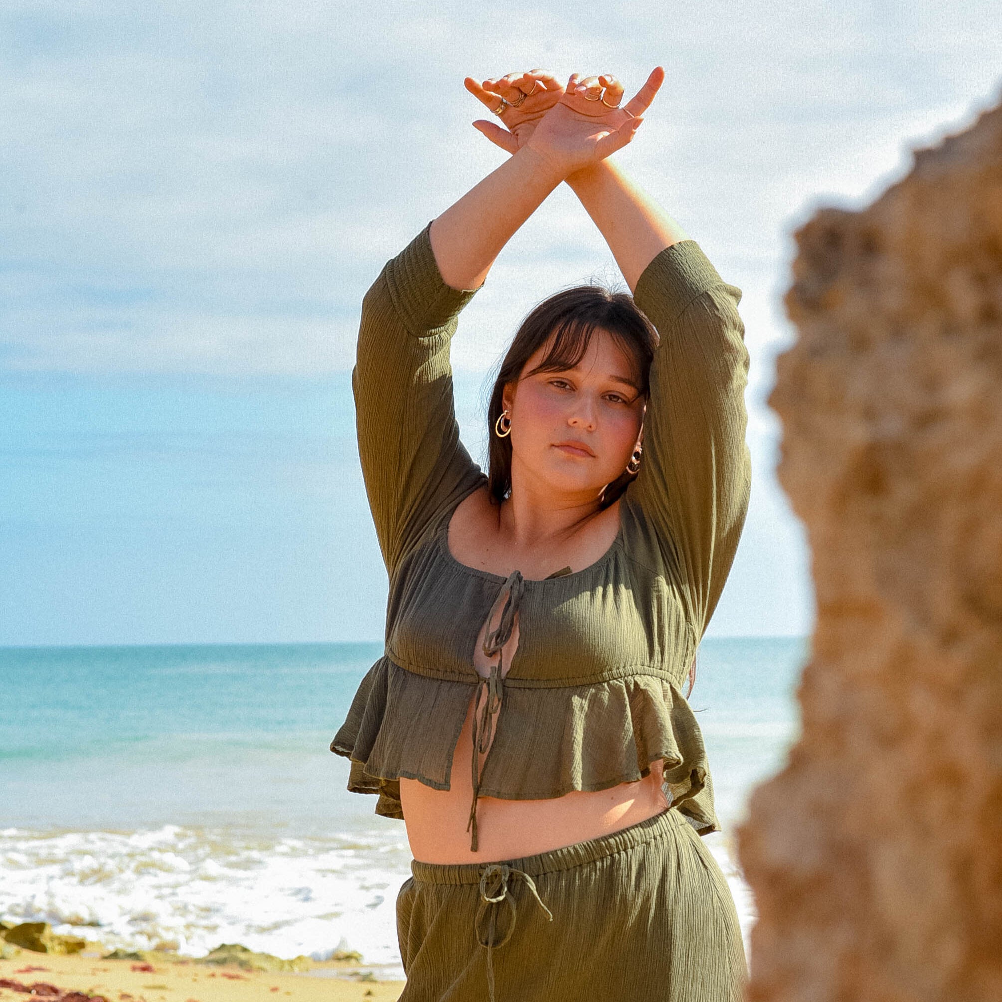 Woman in green outfit standing on a beach with ocean view