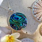 Necklace with a colorful pendant on a textured surface with a flower and shell.